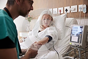 Male Nurse Taking Mature Female Patients Blood Pressure In Hospital Bed With Automated Machine
