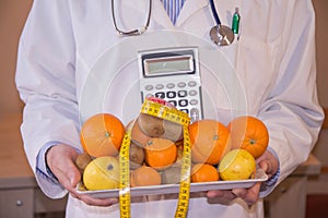 Male nutritionist holding fresh fruits, calculator while standing