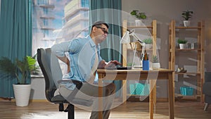 a male office worker or freelancer is sitting on a chair and experiencing back pain