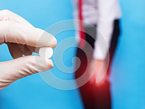 Male office worker holds sore knee joint, pain and inflammation in knee, doctor holds pill, blue background, arthrosis