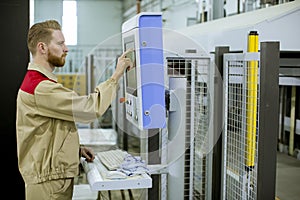 Male operator presses the button on the control panel at the control devices in the furniture production facility