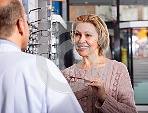 Male optician helps a woman choose spectacles near the display