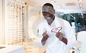 Male optician standing and offering glasses in shop