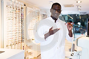 Male optician standing and offering glasses in shop