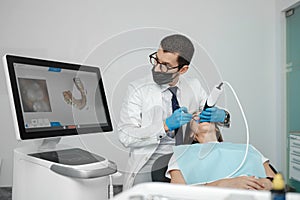 Male orthodontist scaning patient with dental intraoral scanner and controls process on screen.