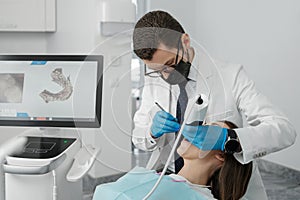 Male orthodontist scaning patient with dental intraoral scanner and controls process on screen.