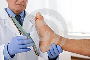 Male orthopedist fitting insole on patient`s foot in clinic