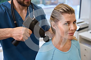 Male osteopath massaging patient with gun to get rid of discomfort in body