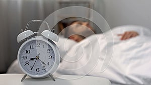 Male oversleeping in morning, alarm ringing at night table, time management