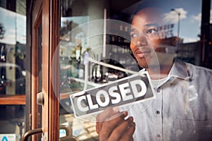 Male Owner Of Coffee Shop Or Restaurant Turning Round Closed Sign On Door Of Failed Business