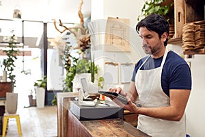 Male Owner With Digital Tablet Standing Behind Sales Desk Of Florists Store
