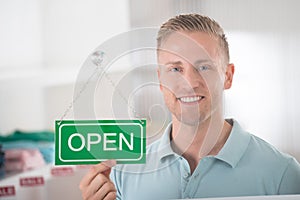 Male Owner Holding Open Sign In Clothing Store