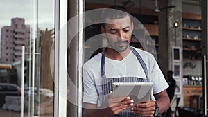 Male owner standing at the doorway of his cafe holding digital tablet