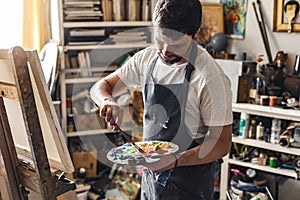 Male painter at art studio indoors in the process of painting pensive