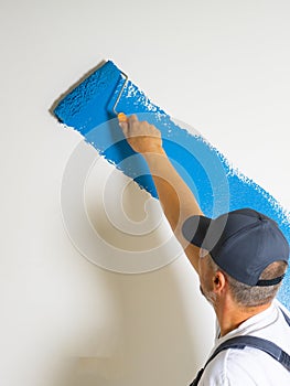 Male painter painting a white wall with a roller in blue color renovations or construction concept