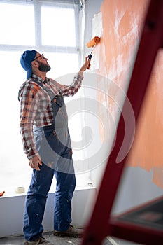 Male painter paints wall with painting roller. Repair, building and home concept. Side view