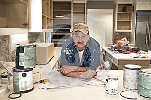 Male painter splattered with paint, holding wet paintbrush in messy home kitchen during remodel with empty paint cans photo