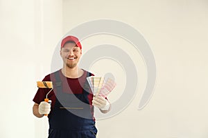Male painter in uniform with color palette samples and roller brush indoors