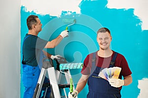 Male painter in uniform with color palette samples and roller brush indoors
