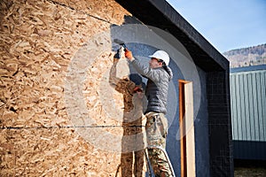 Male painter using paint roller, doing exterior paint work while building wooden frame house.