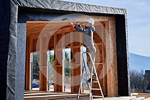 Male painter using paint roller, doing exterior paint work while building wooden frame house.