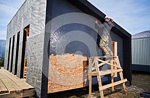 Male painter using paint roller, doing exterior paint work while building wooden frame house.