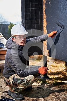 Male painter using paint roller, doing exterior paint work while building wooden frame house.