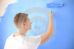 Male painter using roller for refurbishing color of wall indoors