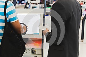 Male passenger with backpack doing self check in for flight at automatic device in modern airport.
