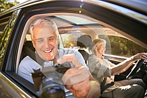 Male Passenger Taking Photo With Camera As Senior Couple Enjoy Day Trip Out In Car 