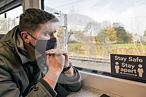 Male passenger wearing face covering mask during covid-19 lockdown inside train in england uk