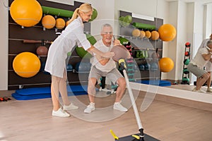 Male patient having a workout with a ball in rehabilitation center with a female instructor