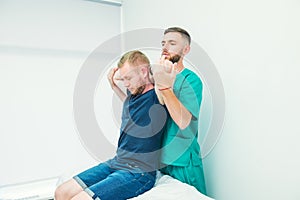 Male patient receiving massage from therapist. A chiropractor stretching his patient`s spine and hands in medical office.