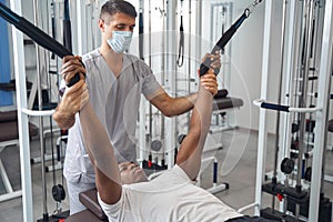 Male patient working out on gym equipment supervised by physiotherapist