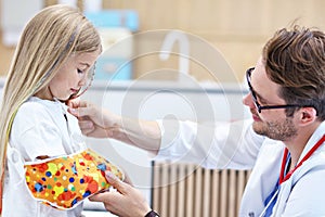 Male pediatrician checking bandage of little girl`s broken arm