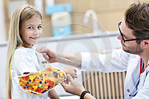 Male pediatrician checking bandage of little girl`s broken arm