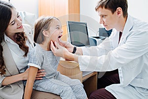 Male pediatrician examining little girl`s tonsils in his office.