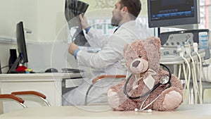 Male pediatrician examining mri scan, plush toy teddy bear on the foreground