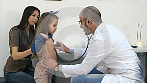 Male pediatrician with stethoscope listening to little girl chest and back photo
