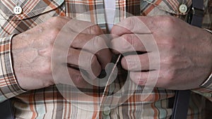 Male pensioner with shaking hands buttoning up shirt, Parkinson tremor disease