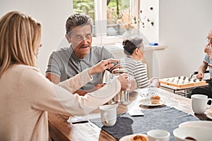 Male pensioner sitting at the table with his caregiver and drinking tea