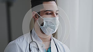 Male pensive thoughtful arab man therapist surgeon wear white uniform medical face mask standing at workplace looking