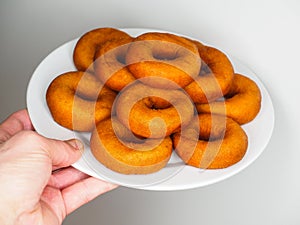 Male person holding a plate of freshly made brown doughnuts
