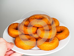 Male person holding a plate of freshly made brown doughnuts