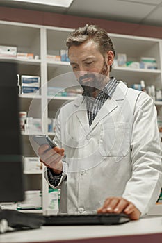 Male pharmacist using the computer and phone while working at the pharmacy