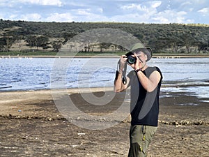 male photographer in a green hat takes a photo the savannah on the background of Lake Nakuru, Kenya. The concept of an