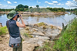 A male photographer in a green hat takes a photo the savannah on the background of river in masai mara, Kenya. concept