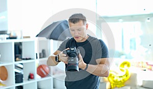 Male photographer holding black professional camera in his hands in studio