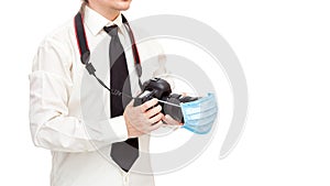 Male photographer in shirt with tie holds camera with a medical protective mask on the lens.