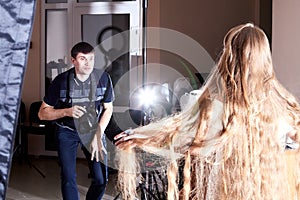 Male photographer taking pictures of model in beautiful shiny dress in photo Studio. Backstage with man and woman during